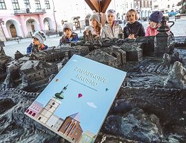 Książczka trzymana w ręce na tle makiety miasta