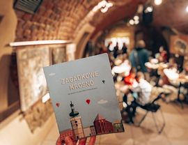 Książczka trzymana w ręce na tle Piwnicy PodCieniami