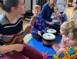 dzieci przyglądają się jak prowadząca warsztaty gra na ukulele