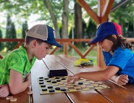 Dwaj chłocy w czapkach z daszkiem rozgrywają partię warcabową