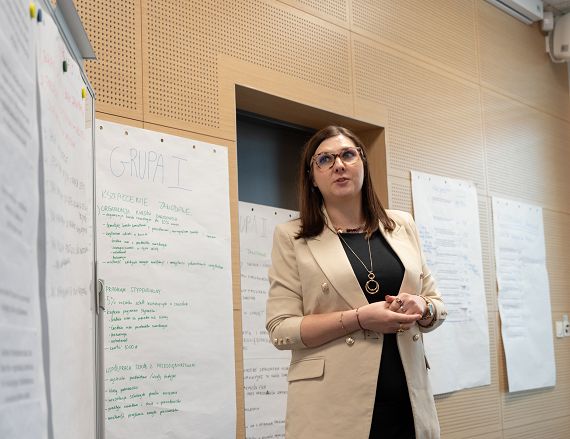 Zdjęcie przedstawia kobietę podczas prezentowania efektów pracy warsztatowej.