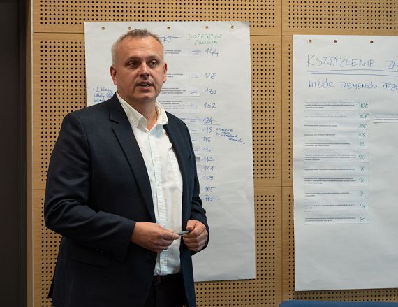 Zdjęcie przedstawia mężczyznę podczas prezentowania efektów pracy warsztatowej.