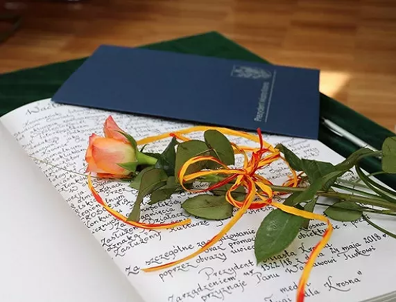 Teczka z listem gratulacyjnym i róża leżącena stole
